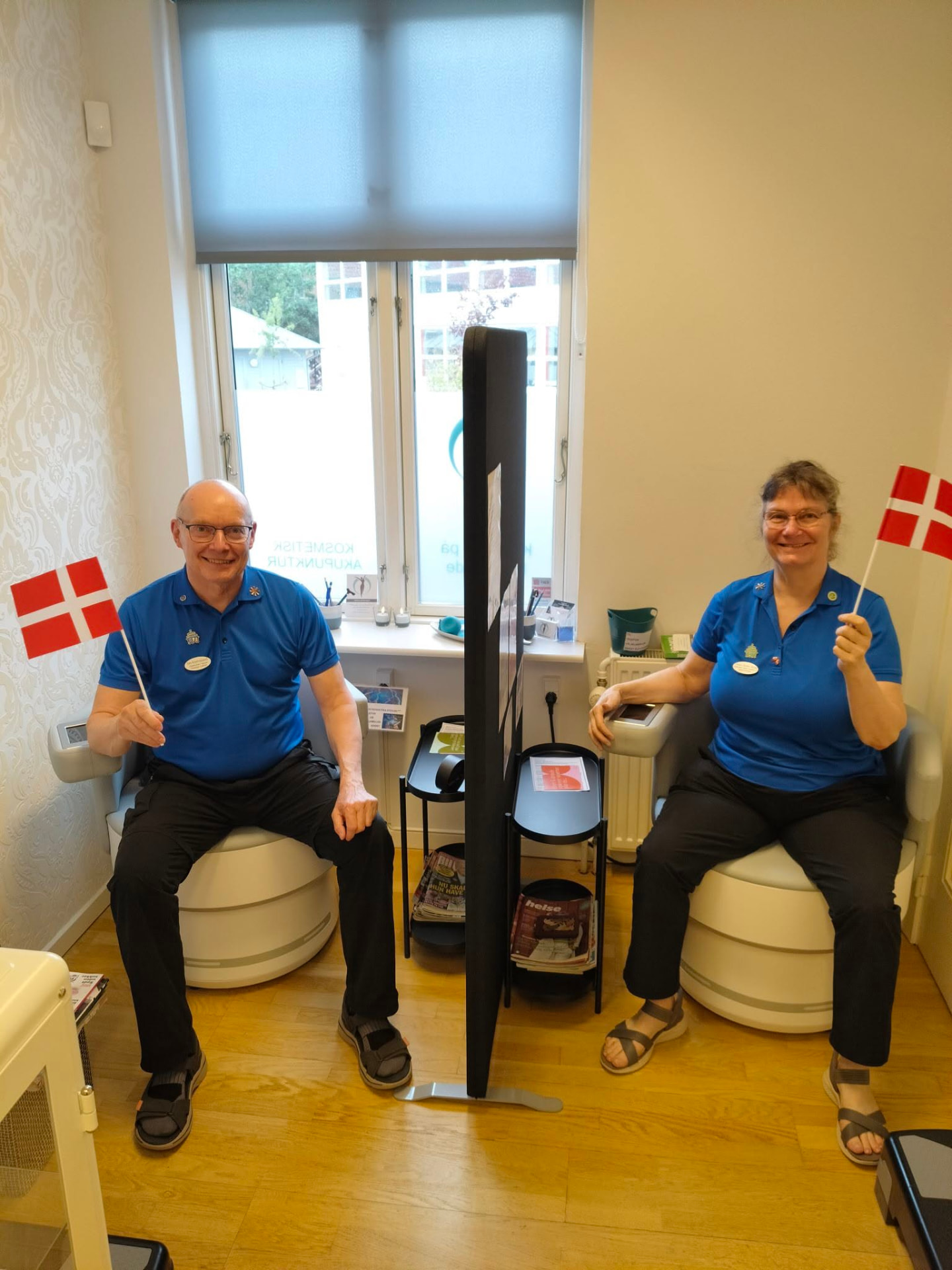 Jan og Anne-Marie sidder i hver sin Pelvic Chair i behandlingsrummet hos Klinikken på Nørregade og holder et Dannebrog